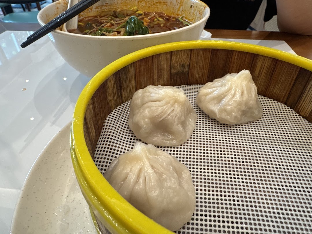 A bamboo steamer with dumplings and a bowl of noodles on a table.