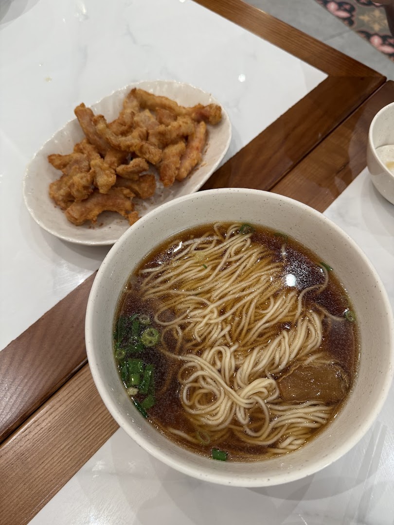 A bowl of noodles and a plate of fried food on a table.