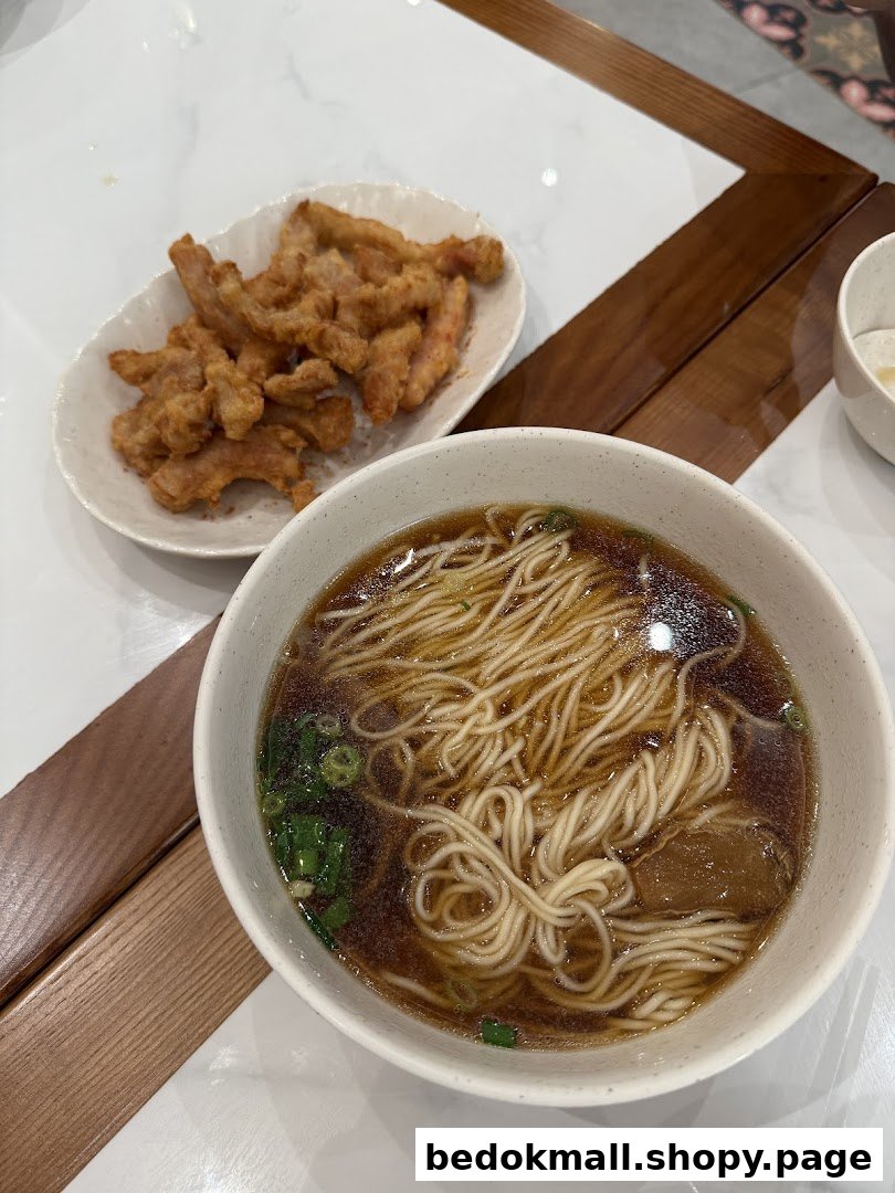 A bowl of noodles and a plate of fried food on a table.