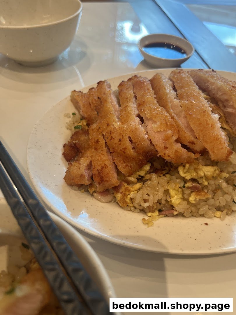 Plate of fried rice with sliced fried meat, chopsticks, and a sauce bowl.