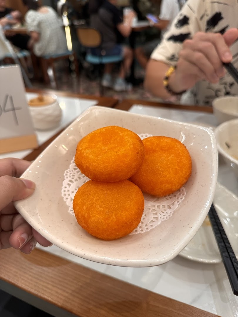 A hand holds a plate with three orange fried buns in a restaurant setting.