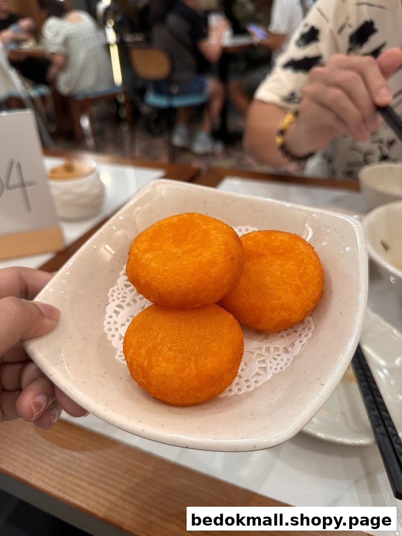 A hand holds a plate with three orange fried buns in a restaurant setting.