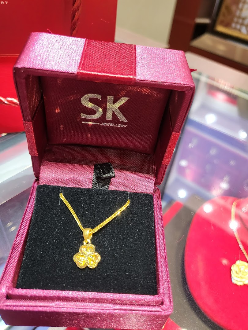 Gold necklace in an open jewelry box with SK Jewellery logo.