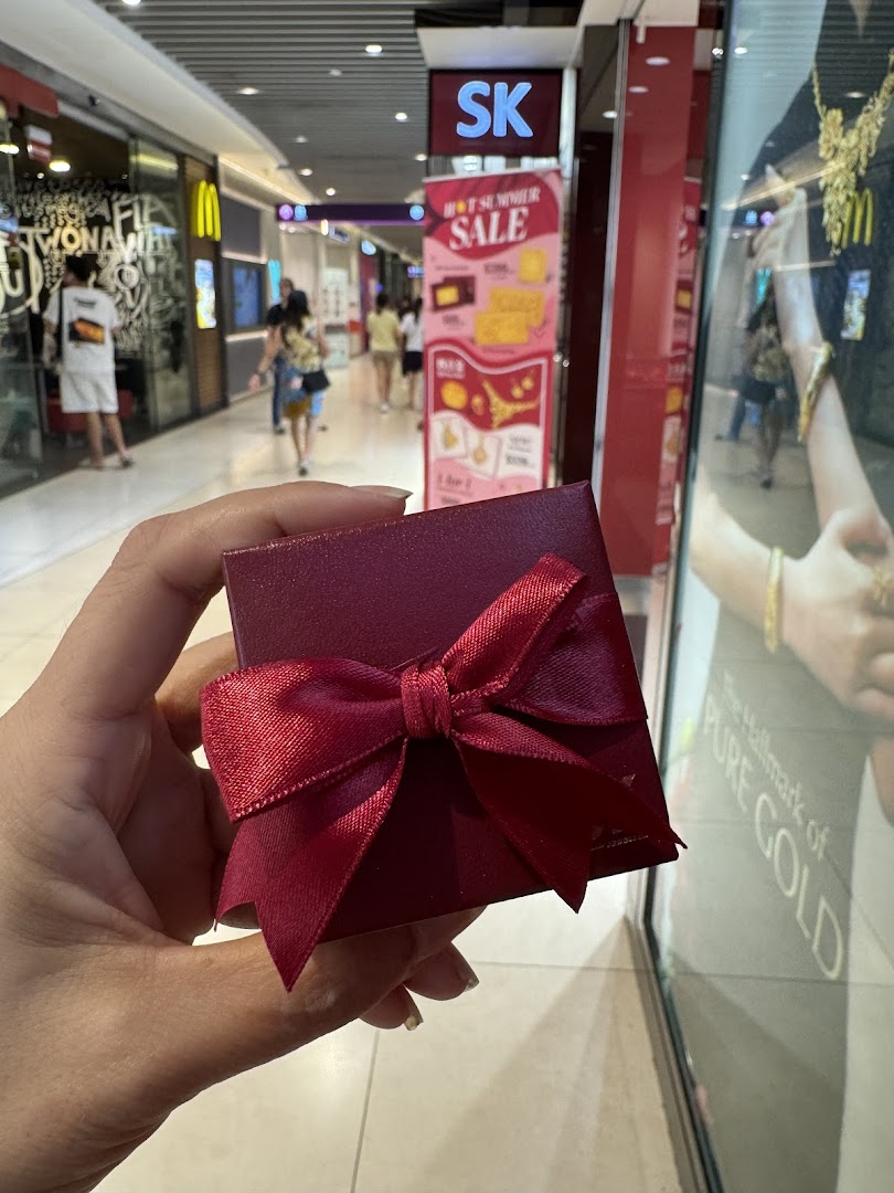 Hand holding a red gift box in a mall corridor with shops in background.