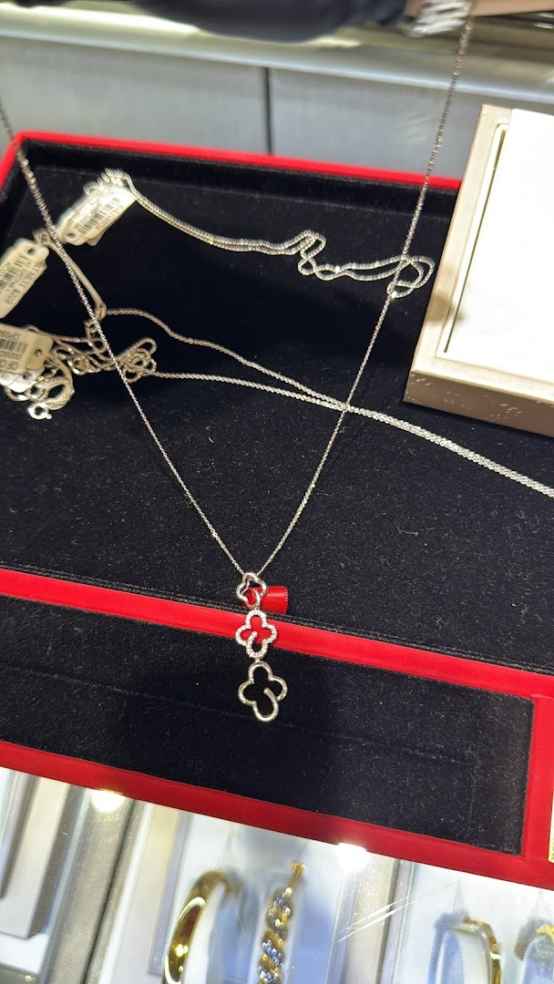 A silver necklace with clover pendants displayed in a red jewelry box.