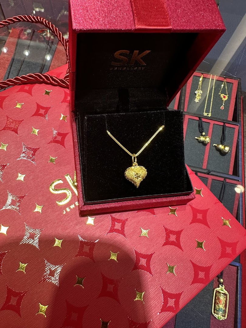 Gold necklace in a red box on a matching shopping bag with other jewelry visible.
