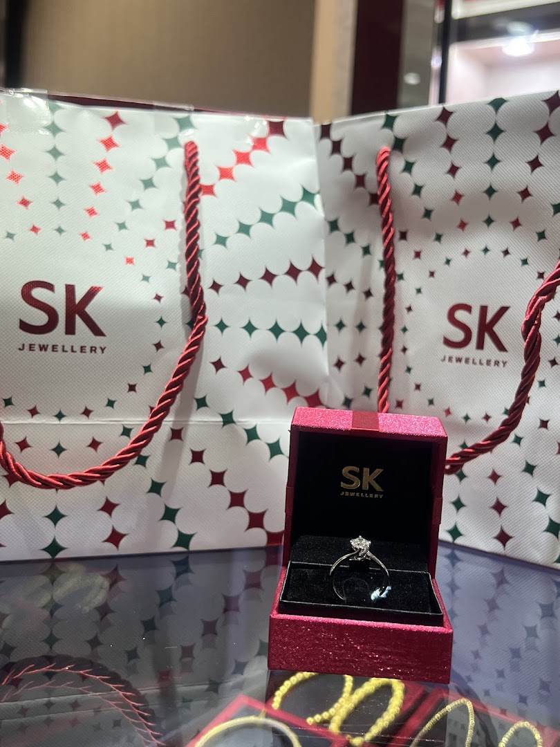 A diamond ring in a red box with SK Jewellery shopping bags on a display.