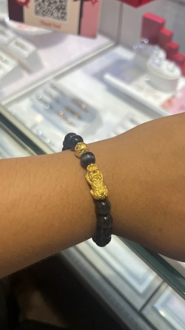 A person's arm wearing a black beaded bracelet with gold charms in a jewelry store.