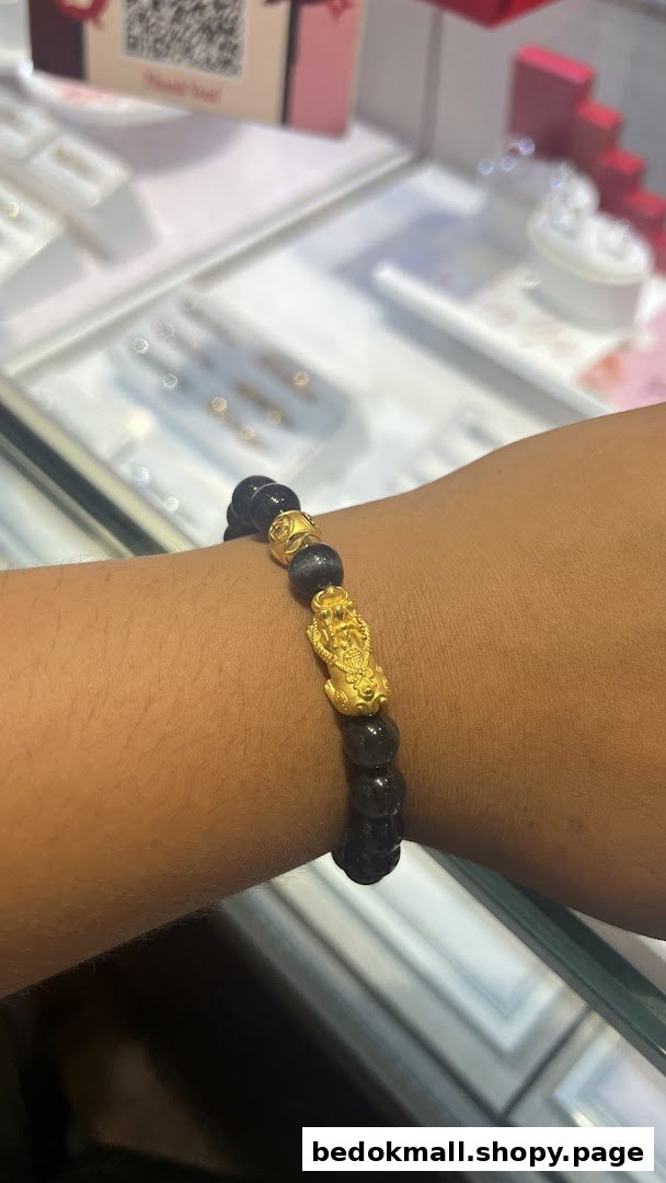 A person's arm wearing a black beaded bracelet with gold charms in a jewelry store.