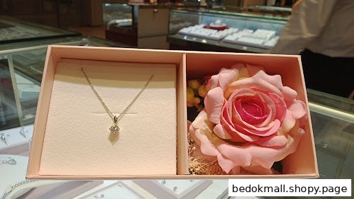 A necklace and pink rose in a gift box, with jewelry displays in background.
