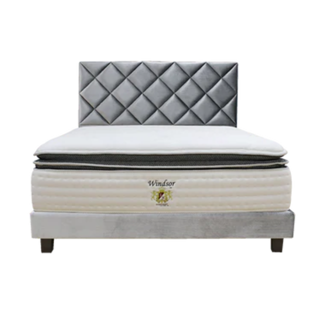 A bed with a white mattress and a grey tufted headboard.