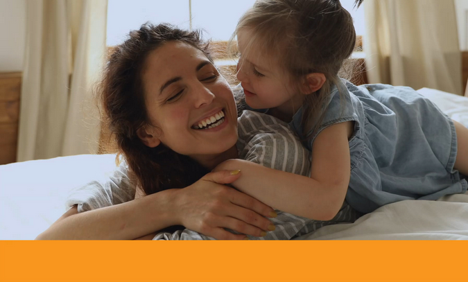 A woman and child are smiling and hugging on a bed.