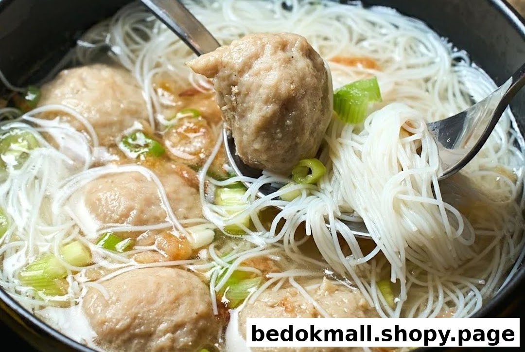 Close-up of a bowl of noodles with meatballs, green onions, and utensils.
