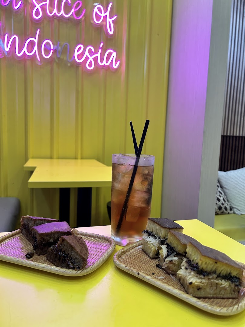 Martabak and a drink on a yellow table with a neon sign in a cafe.