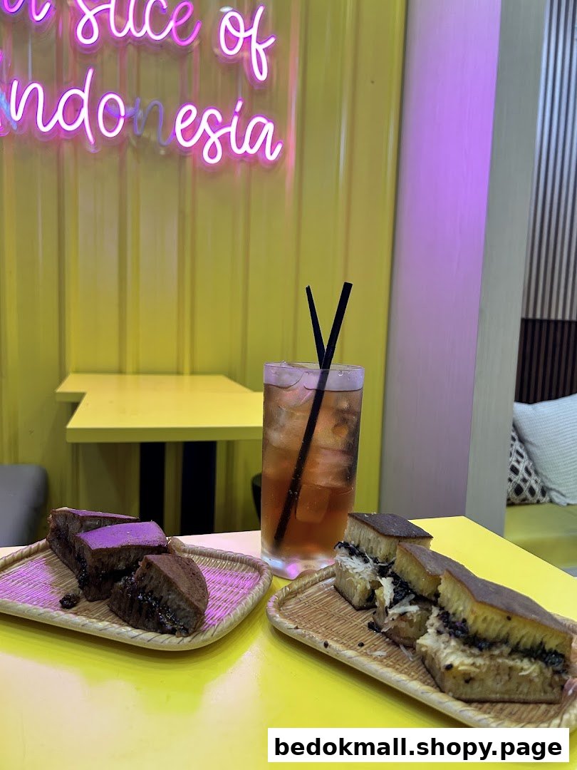 Martabak and a drink on a yellow table with a neon sign in a cafe.