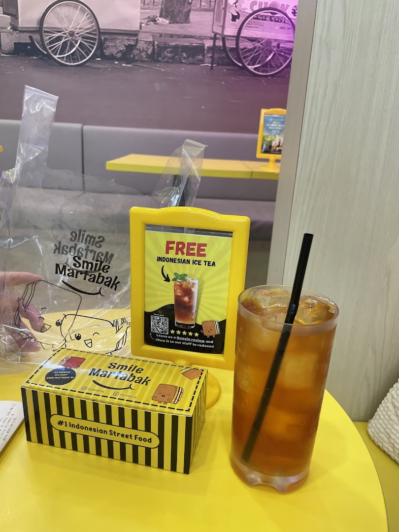 Drink, box, and promotional sign on a yellow table inside a cafe.