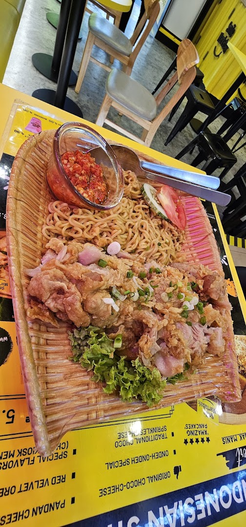 A plate of noodles and fried chicken on a table in a cafe setting.