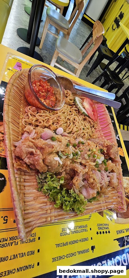 A plate of noodles and fried chicken on a table in a cafe setting.