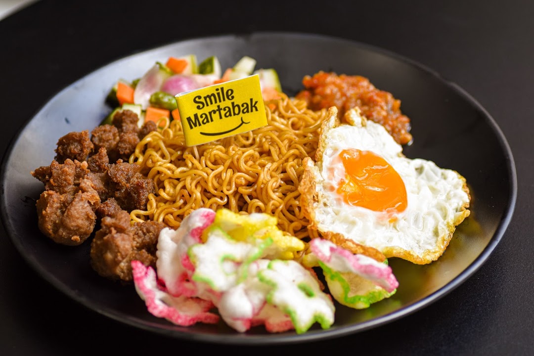A plate of noodles with fried egg, meat, vegetables, and crackers.
