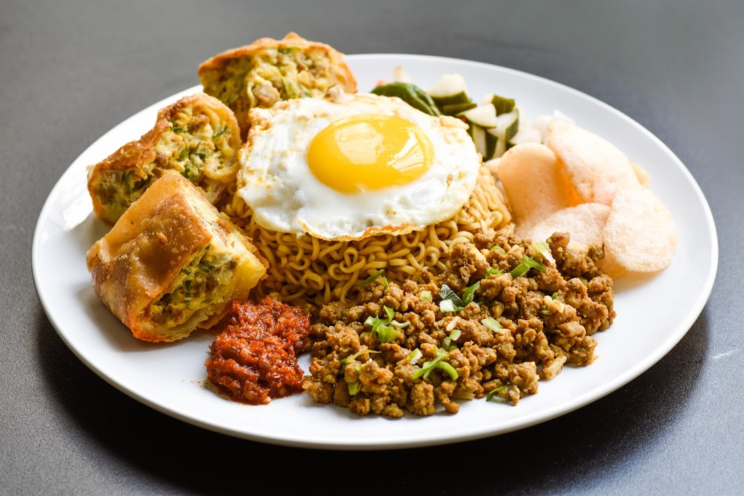 A plate of noodles with fried egg, minced meat, martabak, and crackers.