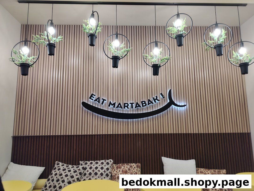 Cafe interior with 'EAT MARTABAK!' sign, decorative lights, and seating area.