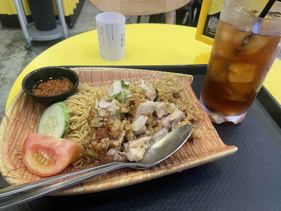 A plate of noodles with chicken and a glass of iced tea on a table.