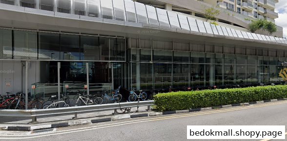 Modern building exterior with glass windows, sidewalk, hedge, and parked bicycles.