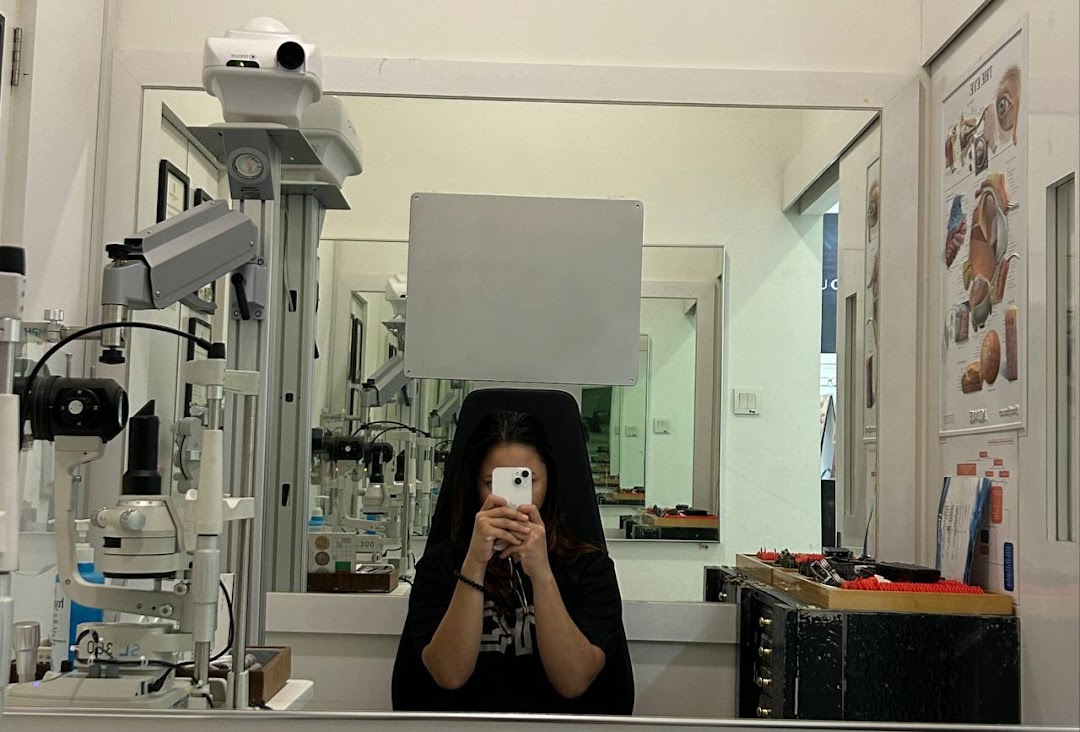 Interior of an optical shop with eye examination equipment and a person taking a mirror selfie.