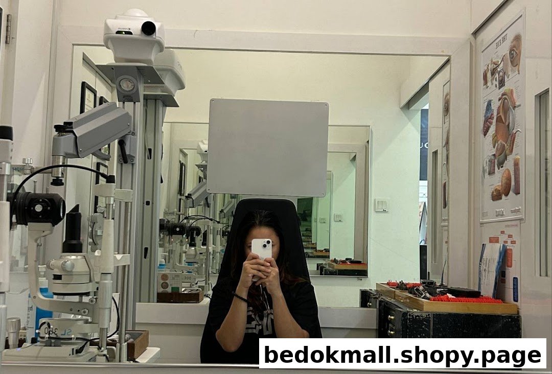 Interior of an optical shop with eye examination equipment and a person taking a mirror selfie.