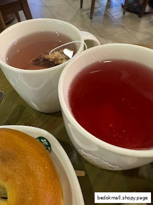 Close-up of two beverages and a bagel on a table.