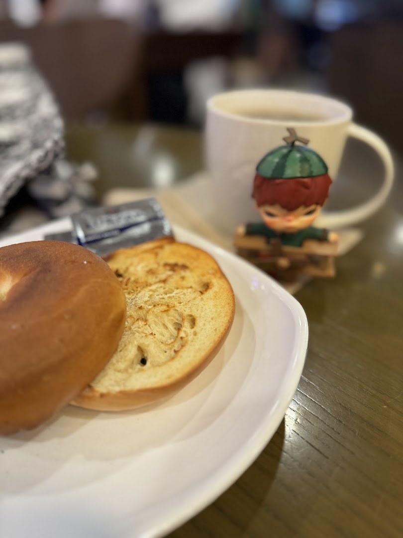 Bagel, butter, coffee cup, and figurine on a table.
