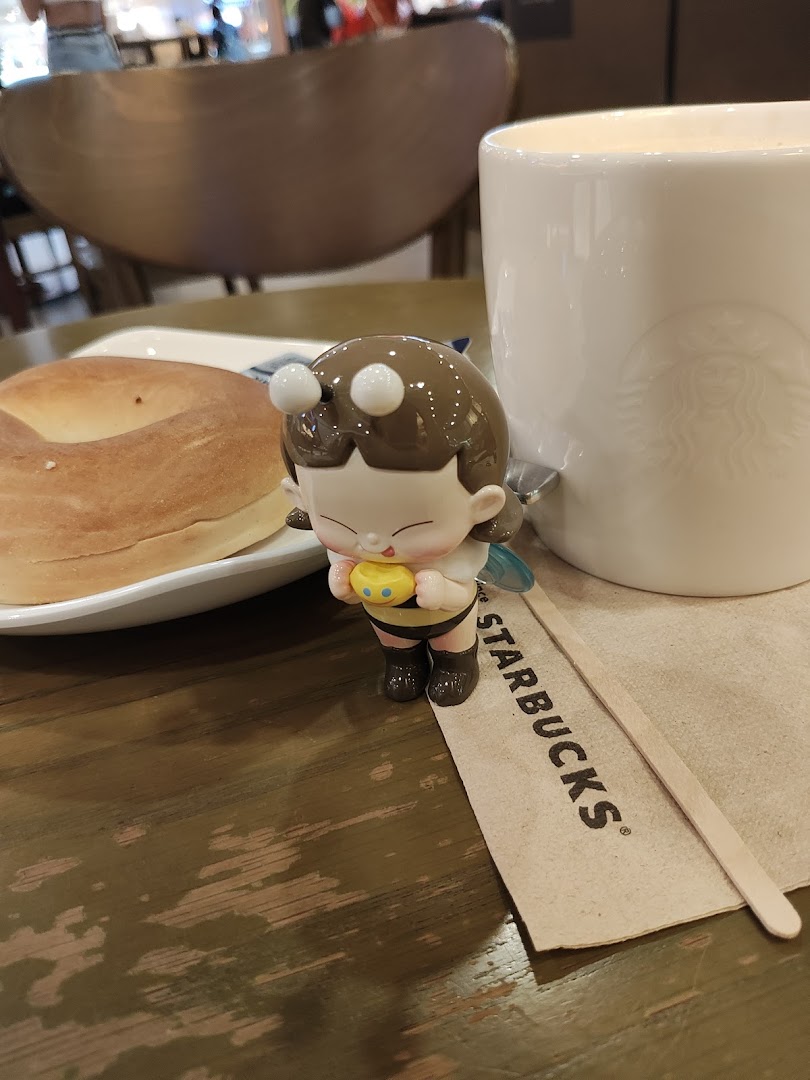 A bagel, Starbucks mug, and bee figurine on a table.