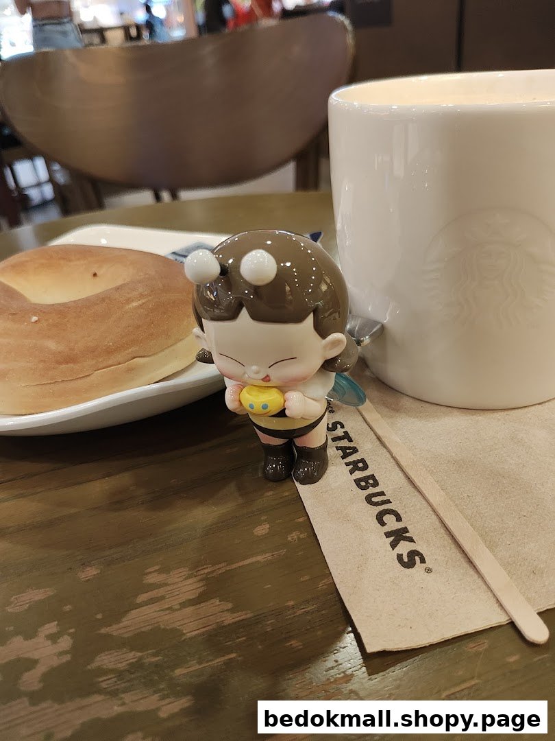 A bagel, Starbucks mug, and bee figurine on a table.