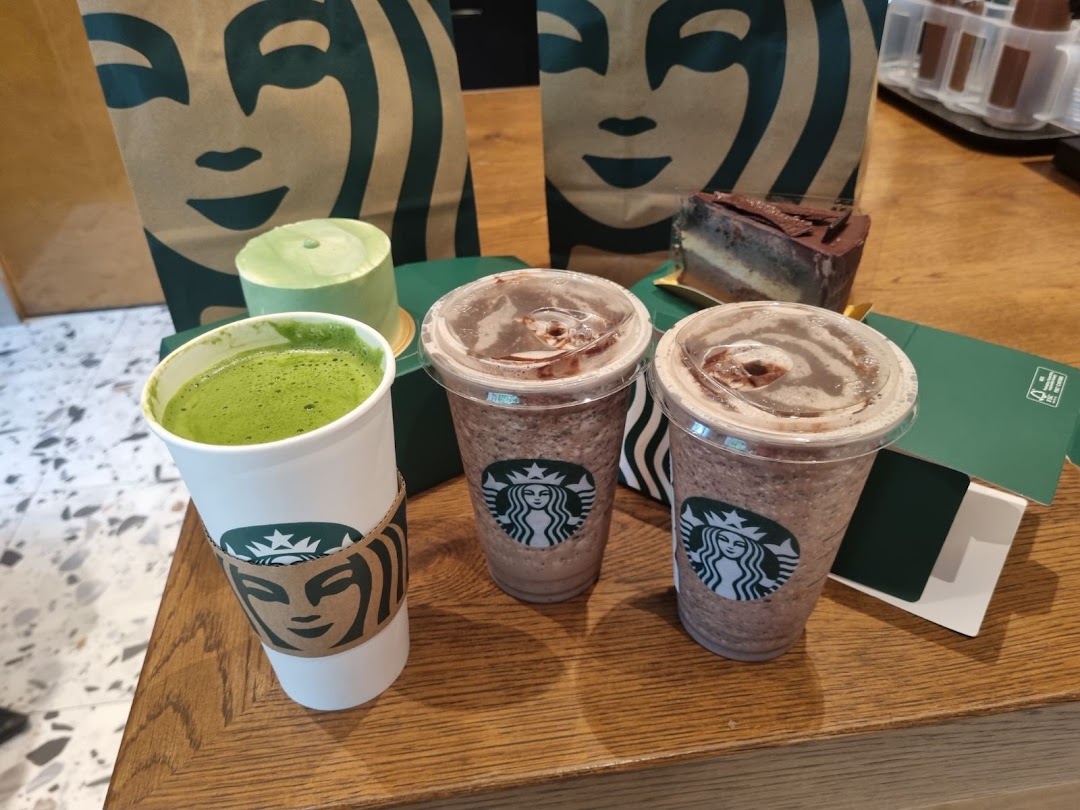 Starbucks drinks and cakes on a wooden table with branded bags.