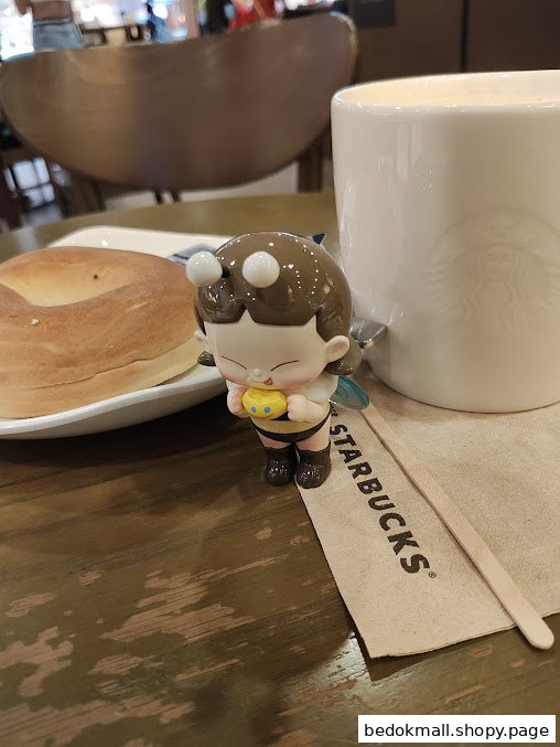A bagel, Starbucks mug, and figurine on a wooden table.