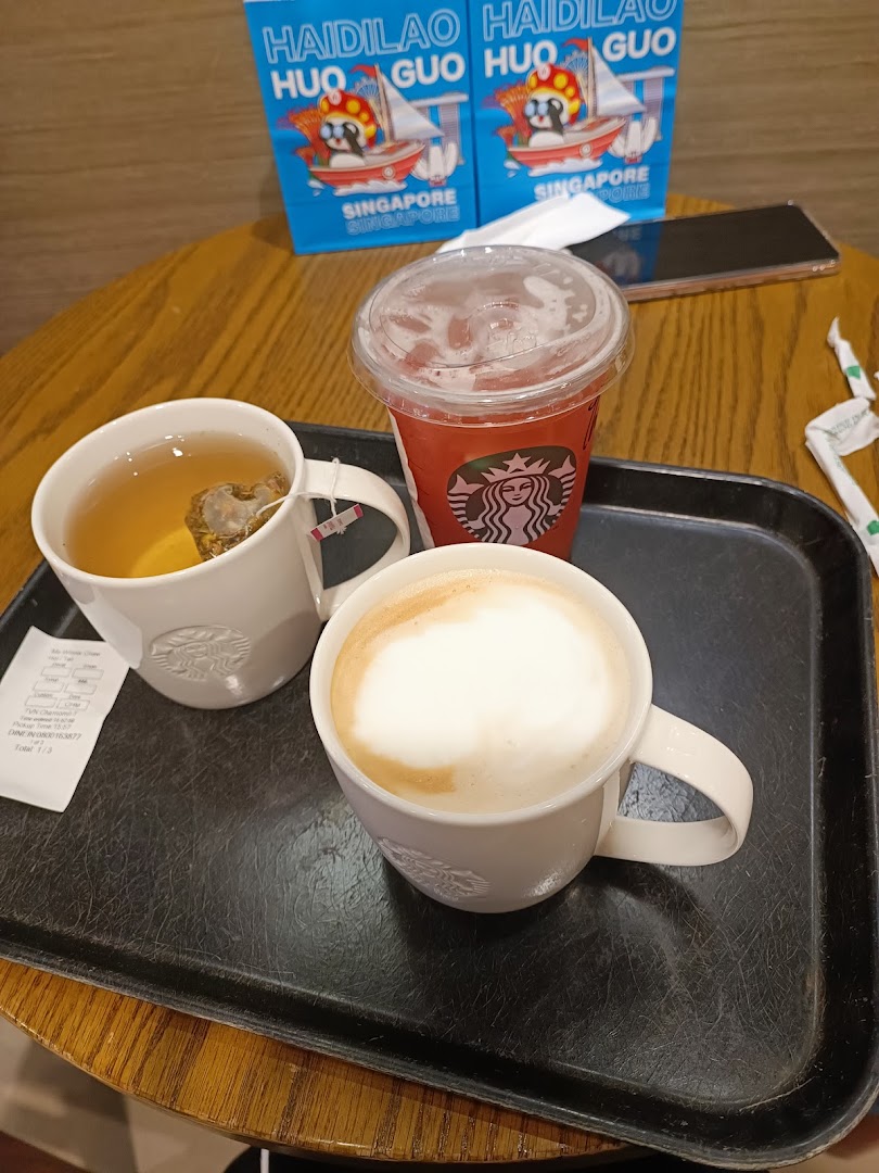 Three drinks on a tray on a wooden table with bags in the background.