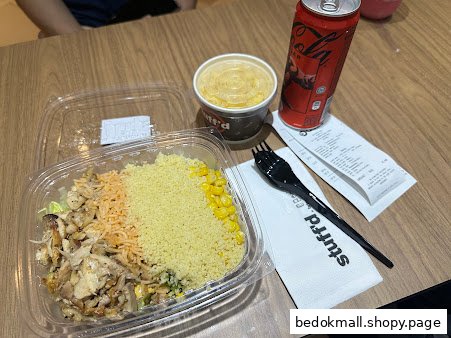 A meal with a salad bowl, drink, and receipt on a wooden table.