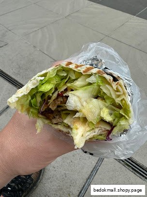 A hand holds a large wrap filled with meat and lettuce.