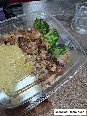 Prepared meal in a plastic container with chicken, couscous, and broccoli.