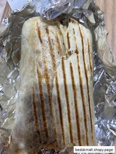A grilled wrap or burrito partially unwrapped from aluminum foil.