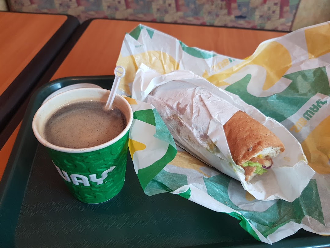 A coffee cup and a Subway sandwich on a green tray.