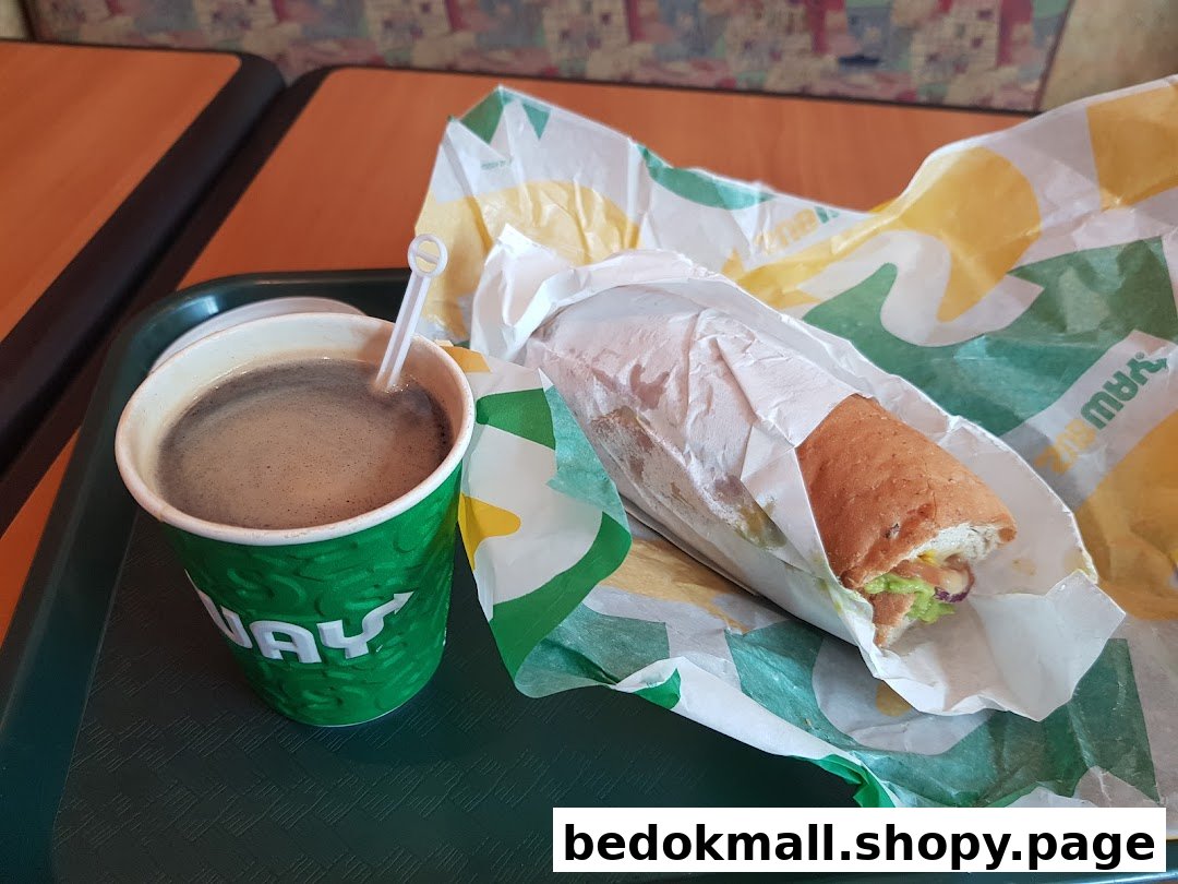 A coffee cup and a Subway sandwich on a green tray.