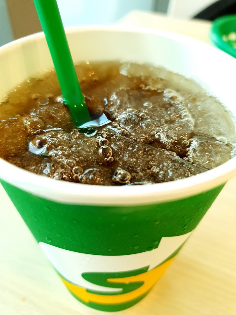 Close-up of a carbonated drink with ice and a green straw in a Subway cup.