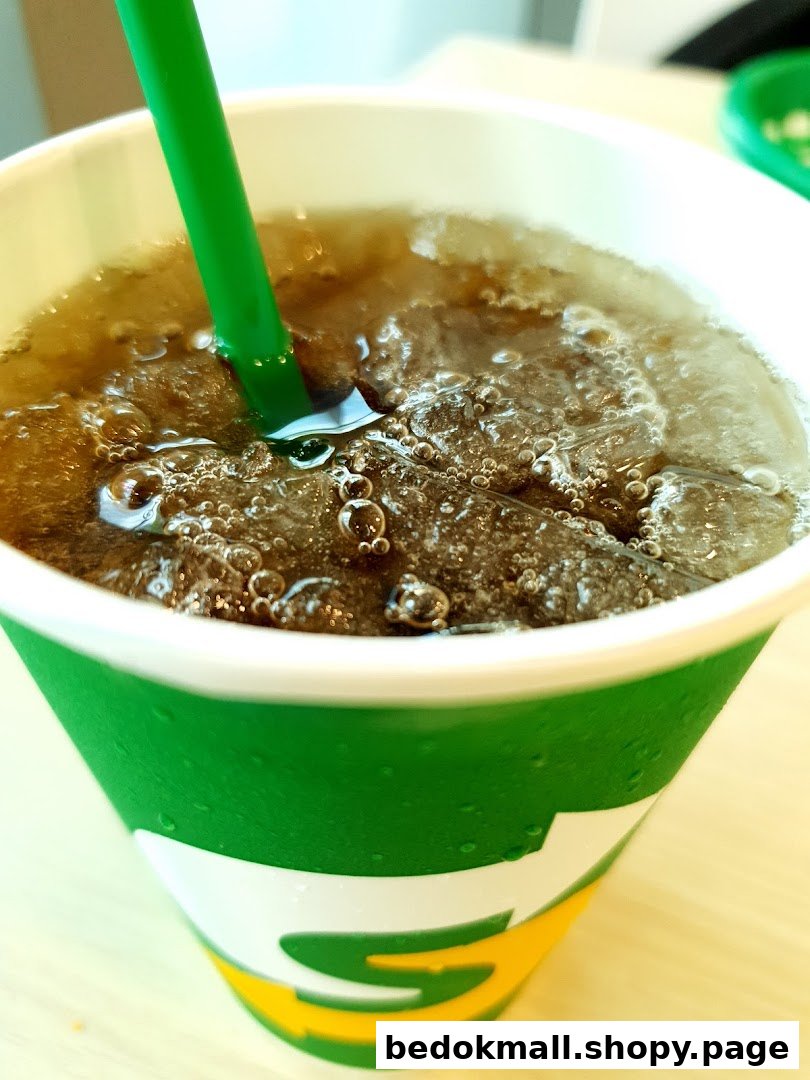 Close-up of a carbonated drink with ice and a green straw in a Subway cup.