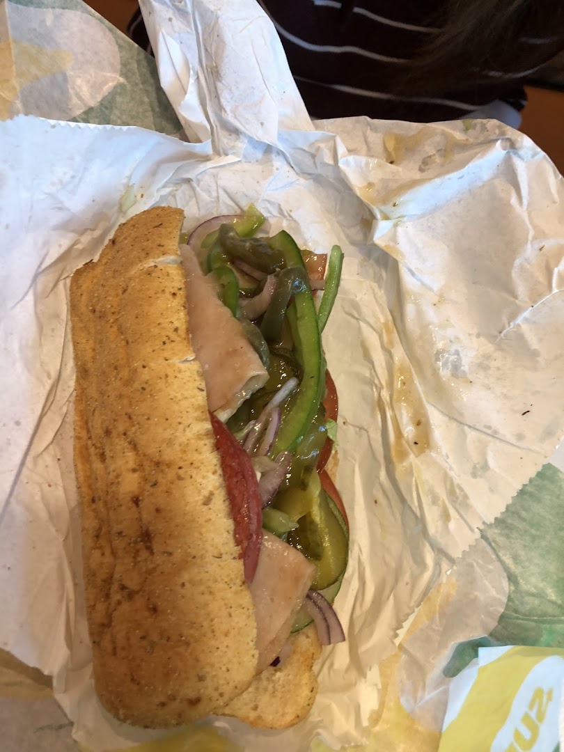 A Subway sandwich with meat and vegetables in paper wrapping.