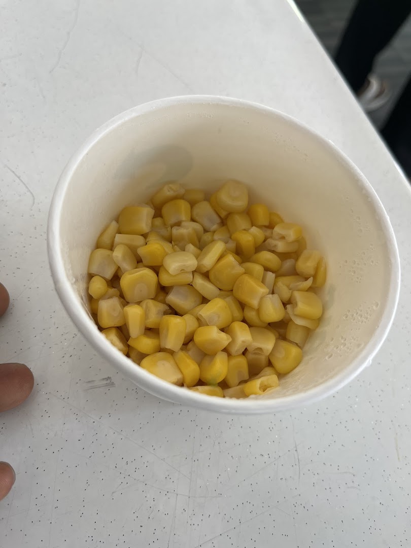 A white cup filled with corn kernels on a white surface.