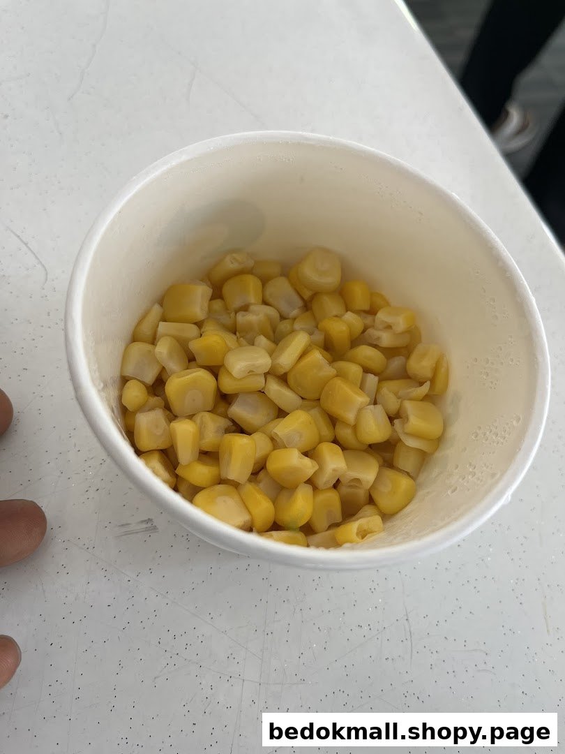 A white cup filled with corn kernels on a white surface.