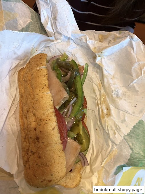 A Subway sandwich with meat and vegetables, partially unwrapped.