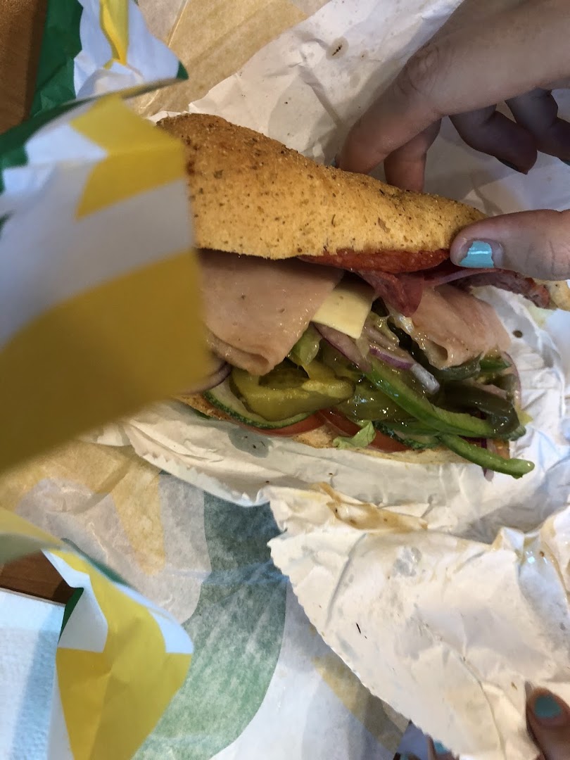 Hands holding a Subway sandwich with the wrapper visible.