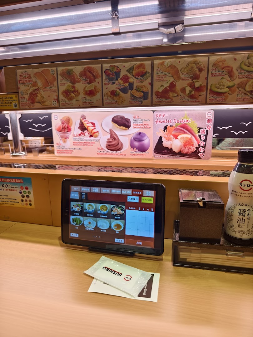 Sushi restaurant interior showing conveyor belt, ordering tablet, and food displays.